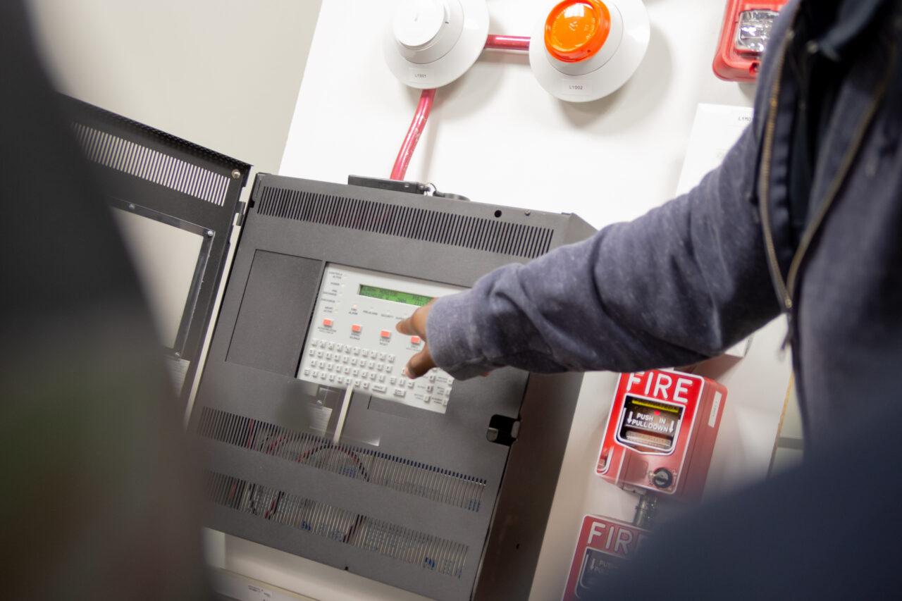 Pull station fire alarm system and mock sprinklers attached to a white wall used for training of security guards.